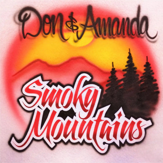 An airbrush design featuring the words 'Don & Amanda' at the top and 'Smoky Mountains' in large stylized red-and-white lettering. The background shows a sunset-style gradient with red, orange, and yellow tones, plus dark tree silhouettes on the right.