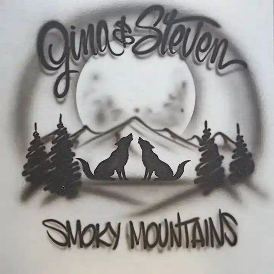 An airbrushed mountain and moon landscape with two howling wolves, flanked by pine trees. The top is personalized with the script 'Gina & Steven' and the bottom reads 'SMOKY MOUNTAINS' in a matching stylized font, all set against a light gray background.