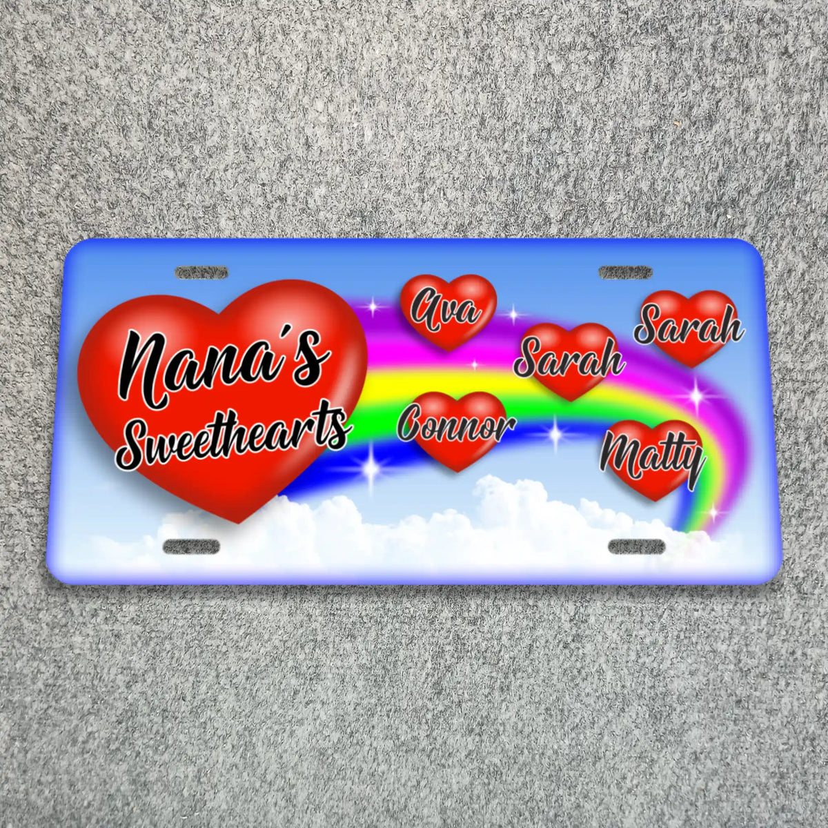 A personalized license plate featuring a blue border, a large red heart reading 'Nana's Sweethearts,' several smaller red hearts with names, and a rainbow over white clouds..