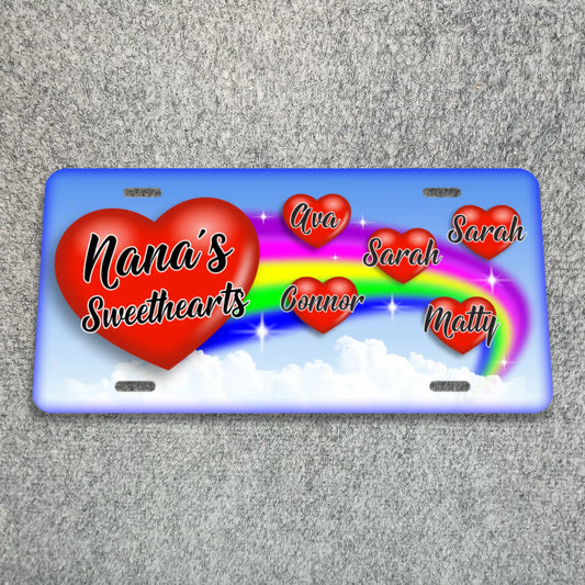 A personalized license plate featuring a blue border, a large red heart reading 'Nana's Sweethearts,' several smaller red hearts with names, and a rainbow over white clouds..