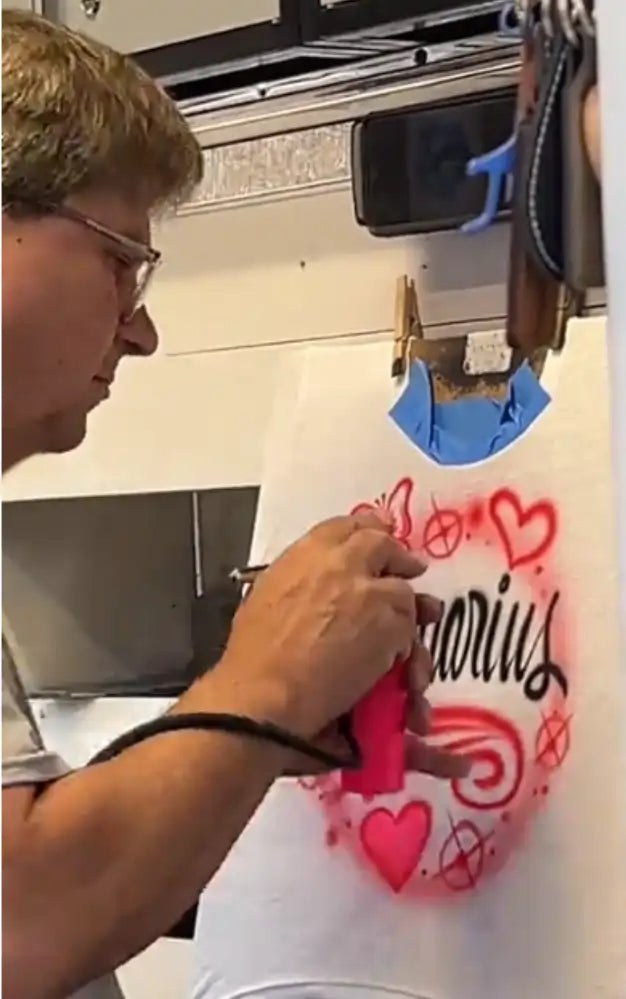 A man airbrushing a white t-shirt with red and black heart and script designs.