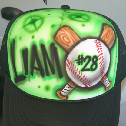 An airbrushed trucker hat with a black mesh back and a vibrant green front panel. The design features the name 'LIAM' in black, a white baseball with red stitching and the number '#28' in black, and two crossed wooden baseball bats.